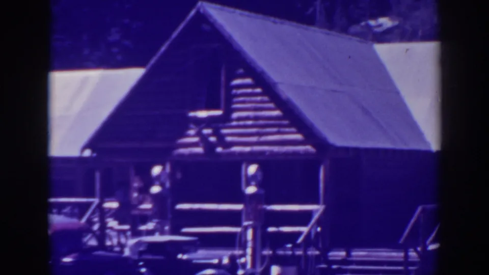 Bucks Lake lodge exterior with log walls, roofline, porch railings, steps, and partial parked cars in aged 8mm color.