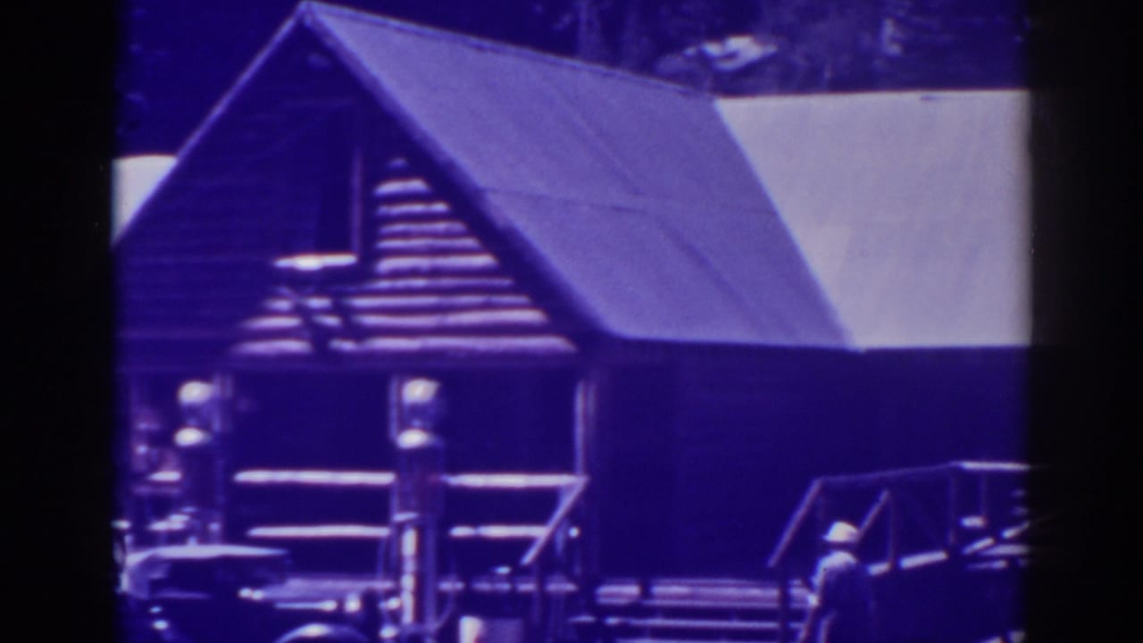 Rustic wooden building with gabled roof, porch railing, steps, and a small figure nearby.