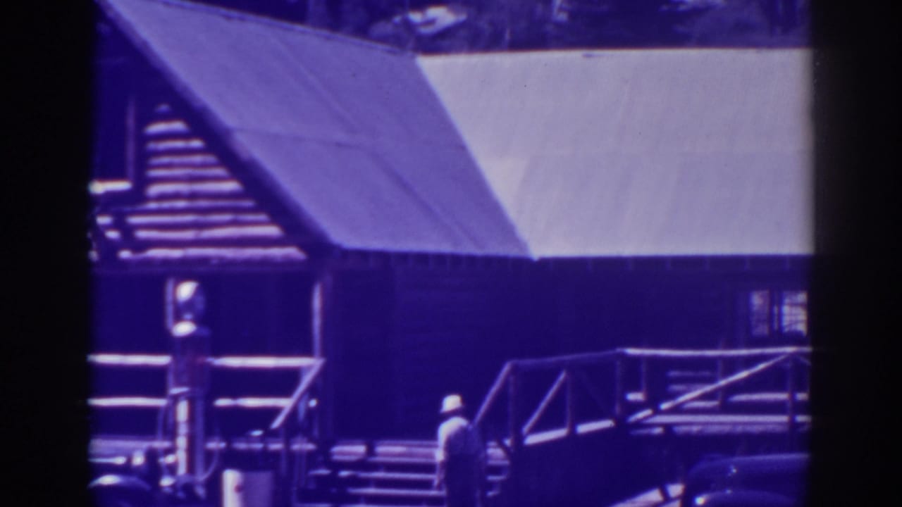 Wooden building facade with railings, steps, a person walking, and part of a vintage car.