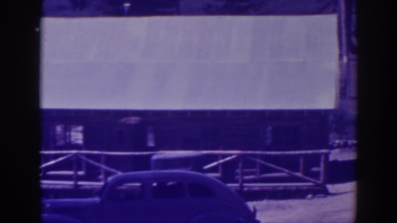 Vintage car parked beside a wooden building and pale rectangular facade.
