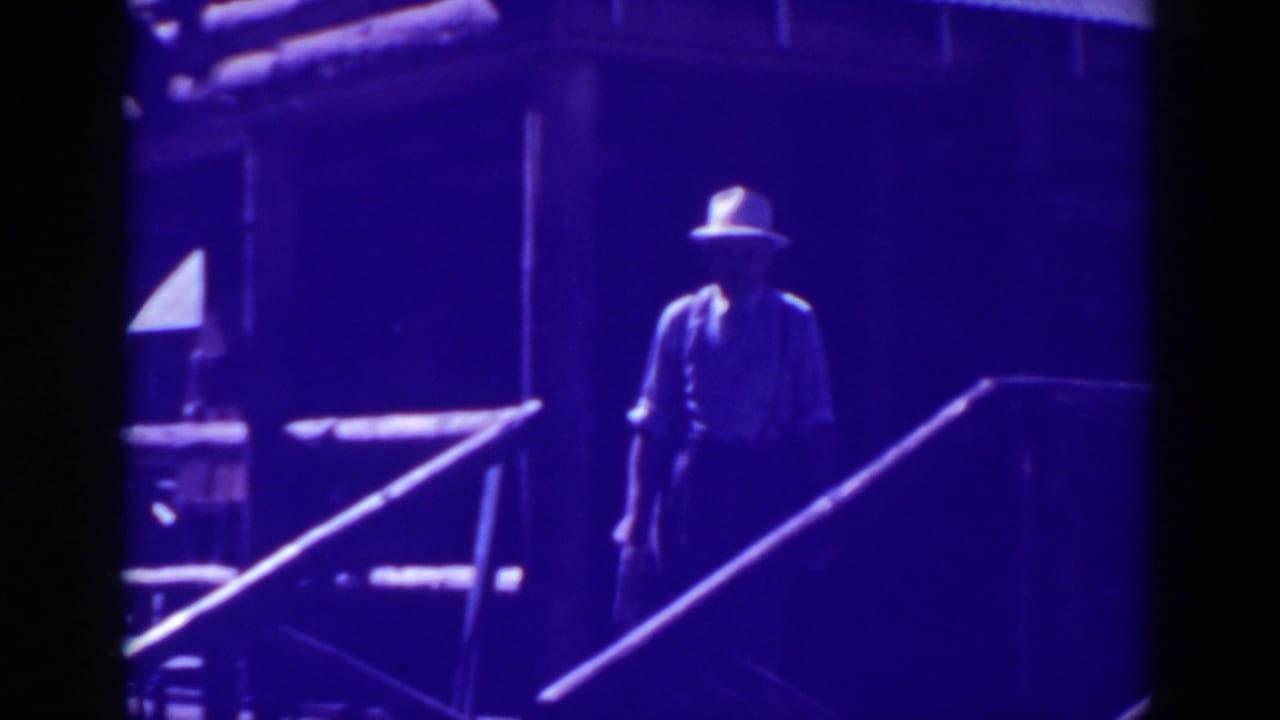 Man in a light hat stands near porch railings and steps.