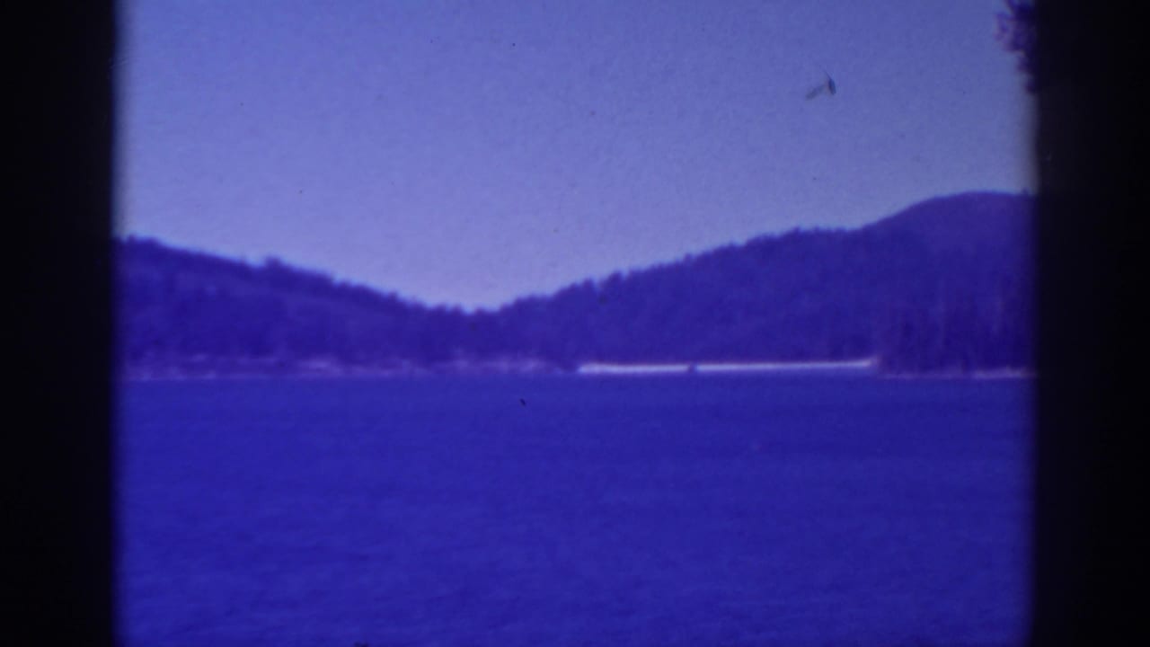 1938 Bucks Lake home-movie frame showing blue water, distant wooded hills, twilight sky, and visible film gate edges.