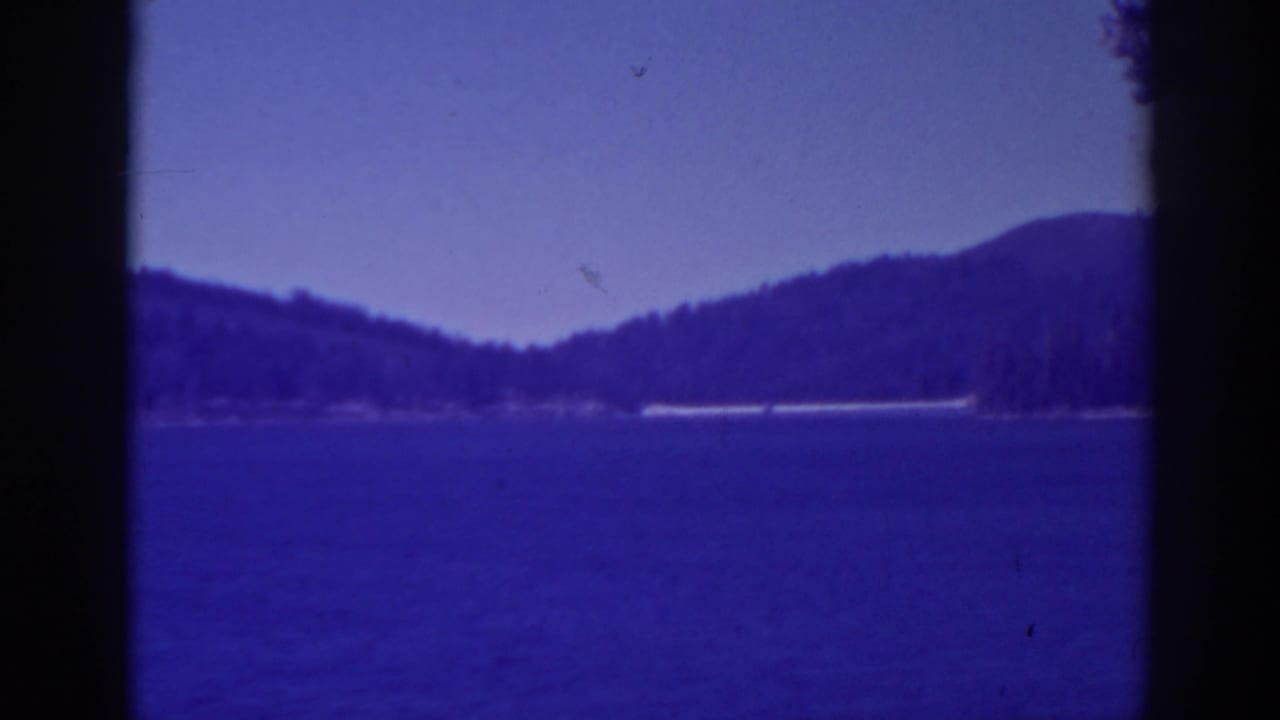 Blue lake and distant forested mountains framed by dark vertical film edges.