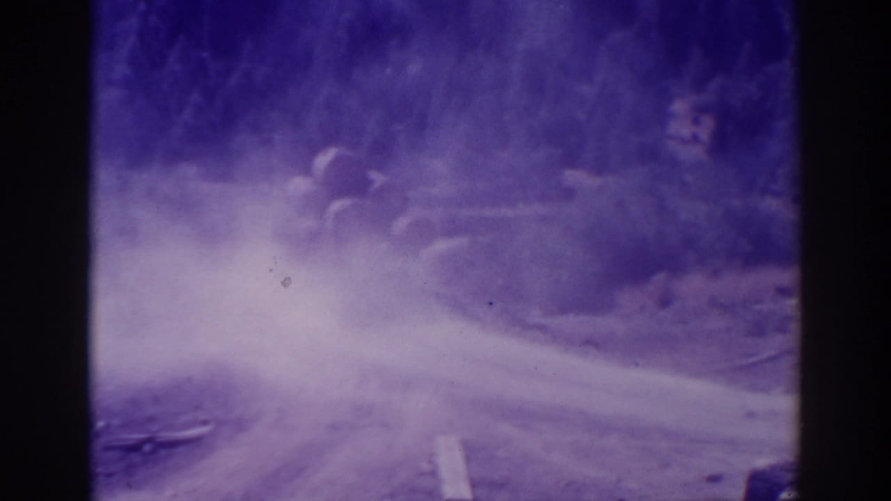 Dusty unpaved road with trees, seen through purple-tinted aged film.
