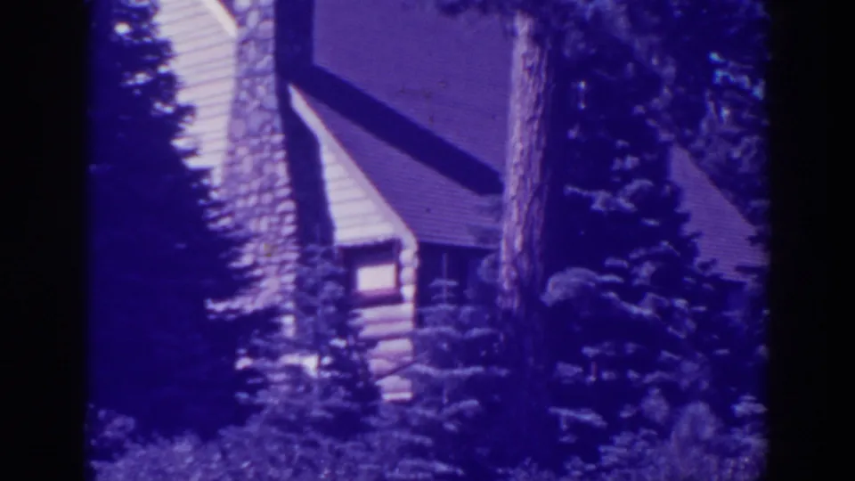 Late-1930s Bucks Lake home-movie frame showing a rustic cabin and stone chimney filtered through pine forest foliage.