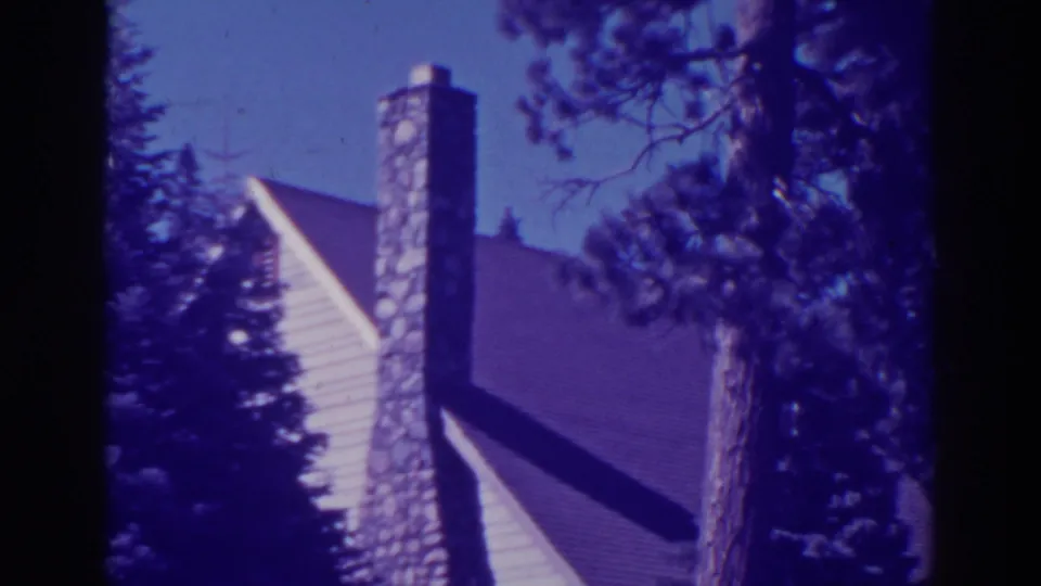 1938 Bucks Lake cabin exterior with a steep roof, prominent chimney, pine trees, and blue-purple aged-film color.
