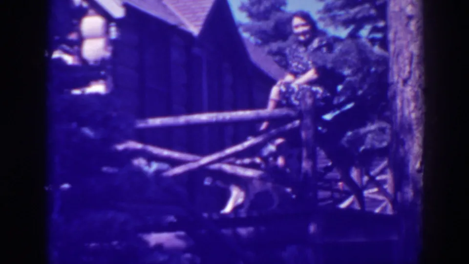 Woman in a dark dress smiles toward the camera from a rustic Bucks Lake cabin porch railing, with a dog below and pines behind.