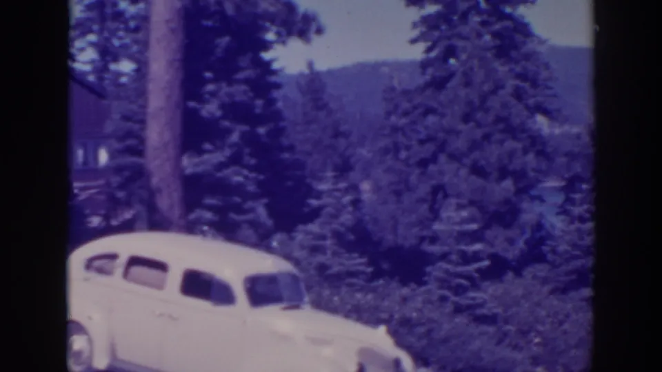 The final frame emphasizes the pale car, tall pines, and forested Bucks Lake hillside, with the cabin partly cropped at left.