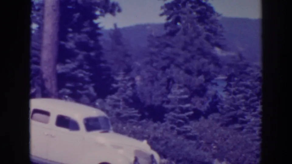 1938 Bucks Lake footage showing a white vintage sedan partly framed by pine forest and distant hills.