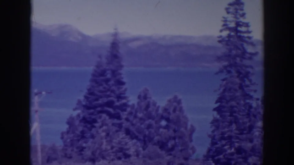 Bucks Lake, California, seen on 8mm film with a tall foreground pine, blue water, distant mountains, and visible film softness.