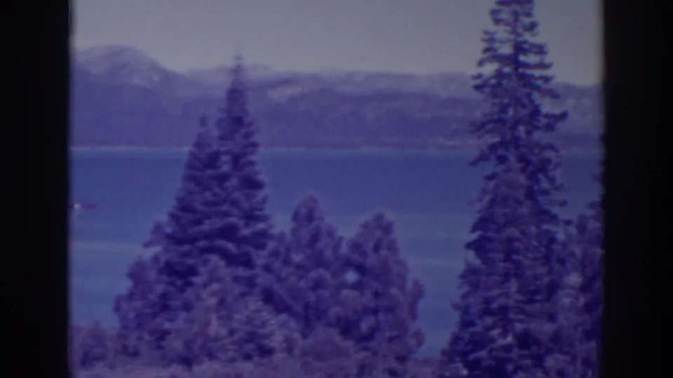 1938 Bucks Lake, California home-movie view through tall conifers toward blue water and distant mountain slopes.