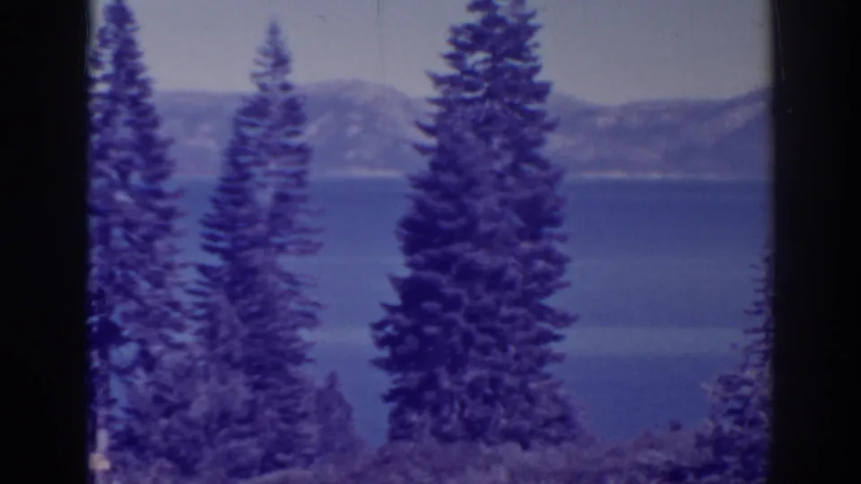 A small-gauge home-movie frame shows Bucks Lake through pines, with blue water and distant California mountain slopes.