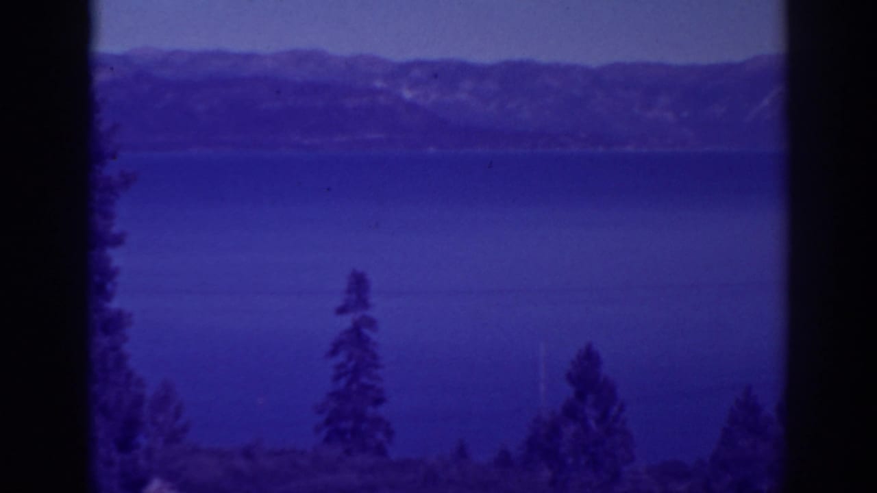 Bucks Lake, California, appears across a steady 8mm view with foreground pines, distant mountains, and soft purple-blue color.