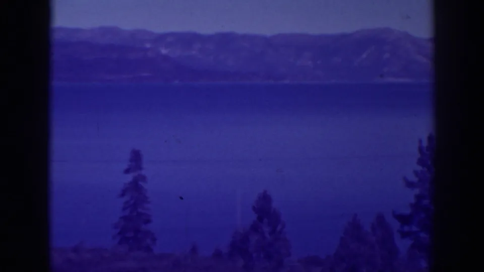 8mm frame from 1938 Bucks Lake footage showing blue water, pine tops, distant ridges, and visible film texture.