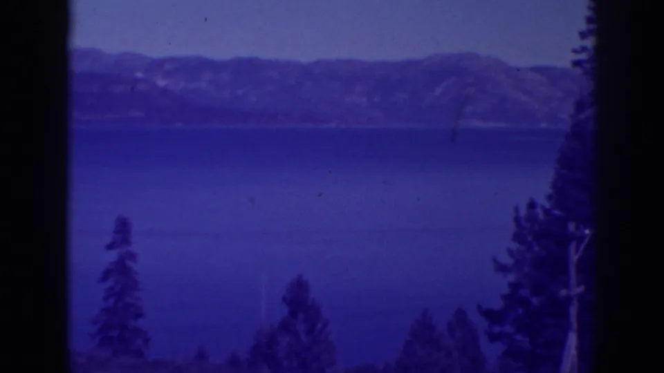 Final Bucks Lake frame shows calm blue water, distant mountain slopes, low pines, and a tall right-edge tree in tinted 8mm color.