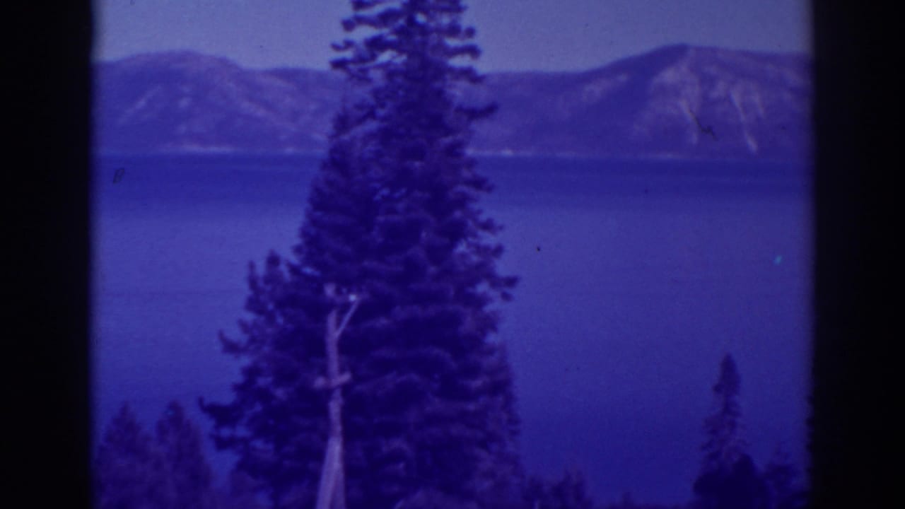 Bucks Lake, California, seen through pine trees with distant mountain slopes under a hazy sky.