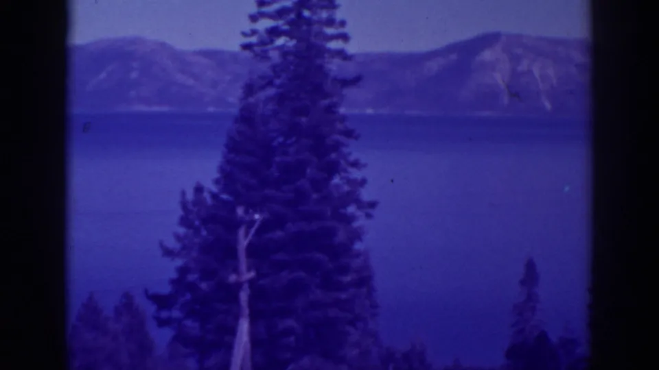 Bucks Lake, California, seen through pine trees with distant mountain slopes under a hazy sky.