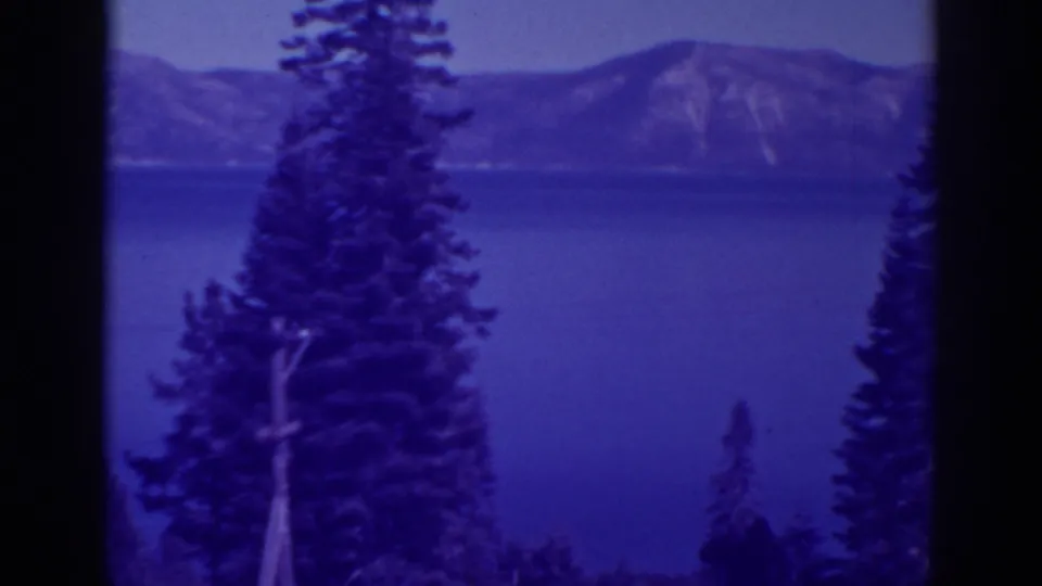 1938 home-movie frame of Bucks Lake with a large pine in the foreground and mountains across the water.