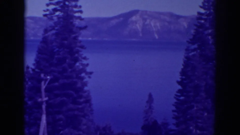 Blue-purple 8mm view of Bucks Lake framed by pines, with distant mountains across the water.