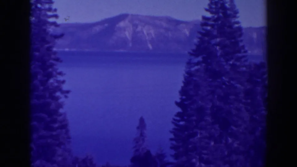Blue-tinted 8mm frame of Bucks Lake scenery, with a calm lake, mountain ridge, and evergreen trees partially blocking the view.