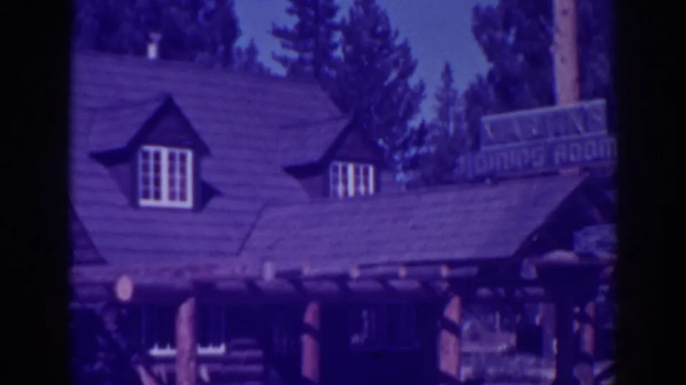 Purple-tinted 8mm exterior view of Martin's Lodge at Lake Tahoe, showing a steep roof, dormer windows, log posts, and pines.