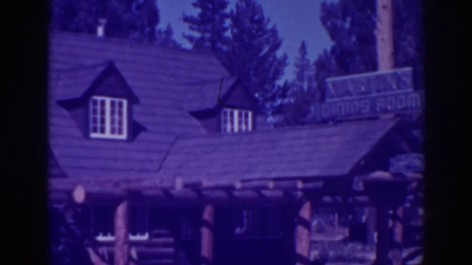 Late-1930s Lake Tahoe lodge exterior from 8mm film, with dormer windows, pine trees, log supports, and a visible dining room sign.
