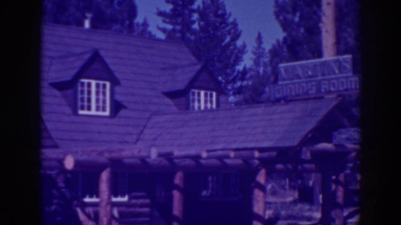Rustic log cabin restaurant with dormer windows, porch posts, and a dining room sign among pine trees.