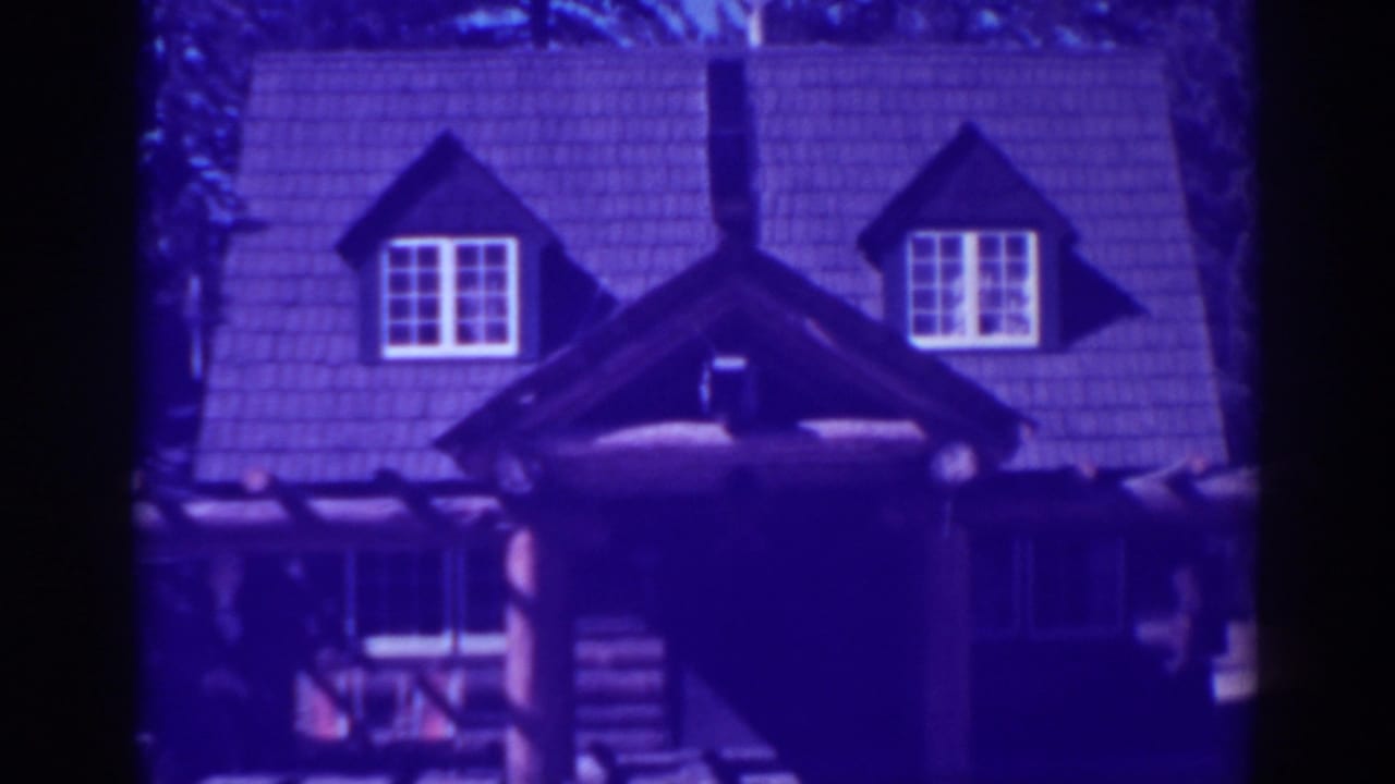 El Dorado City 1938 frame showing the upper facade of a rustic lodge, with twin dormers, white-trimmed windows, and heavy log construction below.