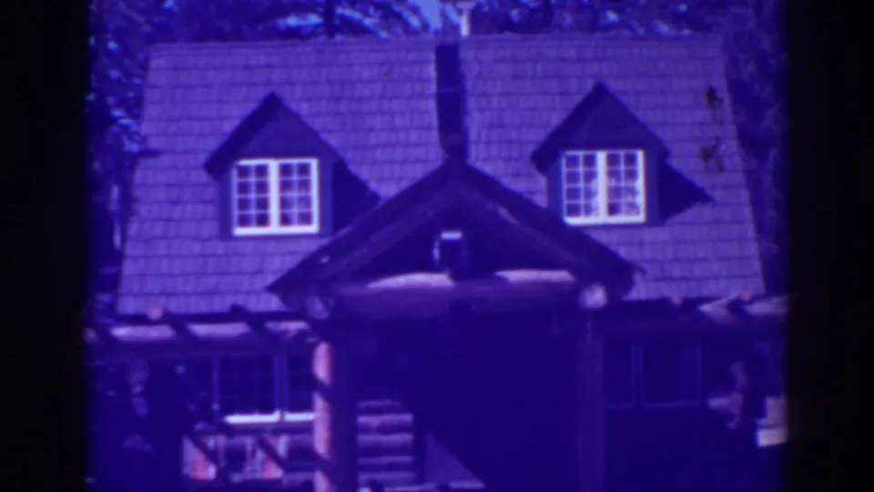 El Dorado City 1938 frame holding on the rustic lodge exterior, with dormers, chimney, shingled roof, log porch, and aged purple-blue film color.