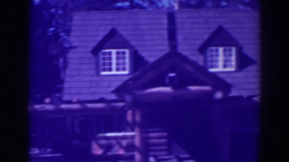 1938 El Dorado City home-movie frame showing a rustic cabin with dormer windows, shingled roof, and shaded porch.