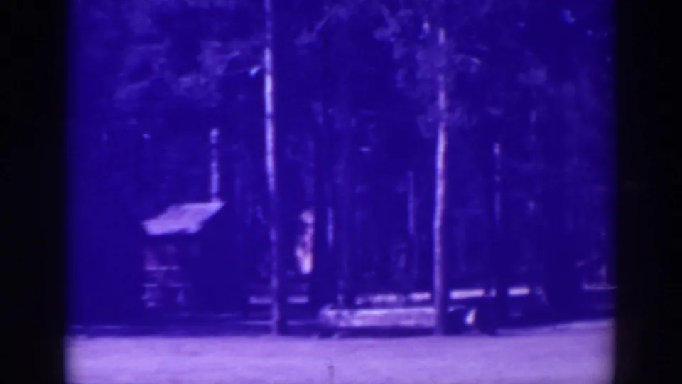 End of the El Dorado City cabin pan, with porch structure, tall trees, and pale ground visible in aged 8mm color.