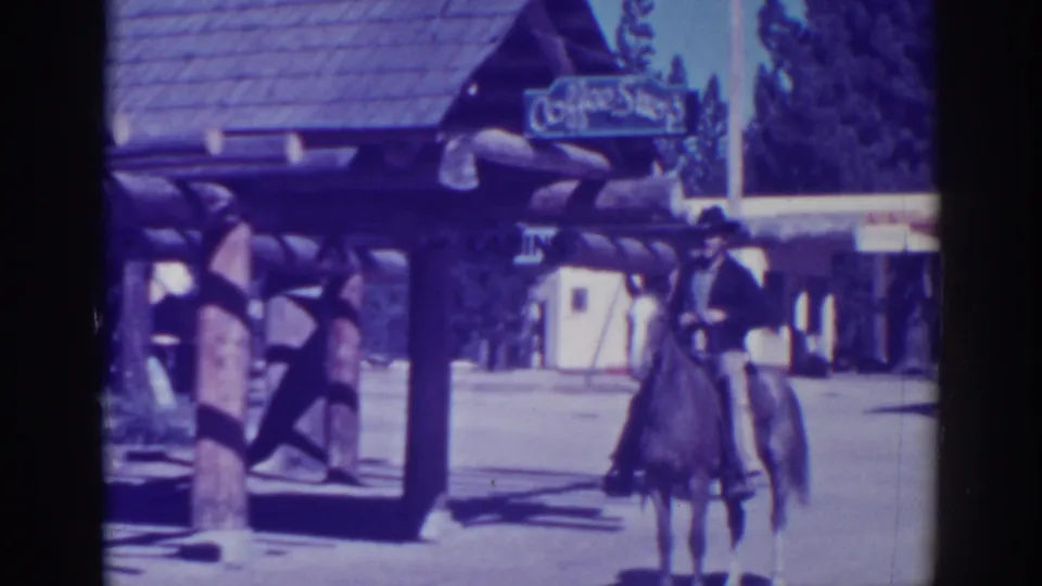 A cowboy-hatted rider on a saddled horse moves away near the Coffee Shop sign and log-style entrance at El Dorado City.