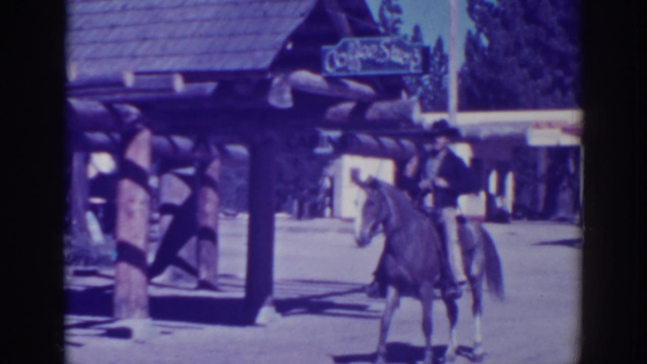Man in a black hat sits on a brown horse near a rustic storefront and Coffee Shop sign.
