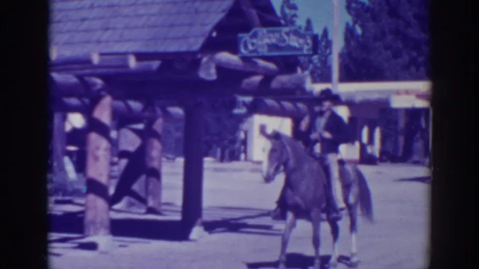 In El Dorado City, California, 1938, a man in Western-style clothing sits on a horse beside a log-style storefront.