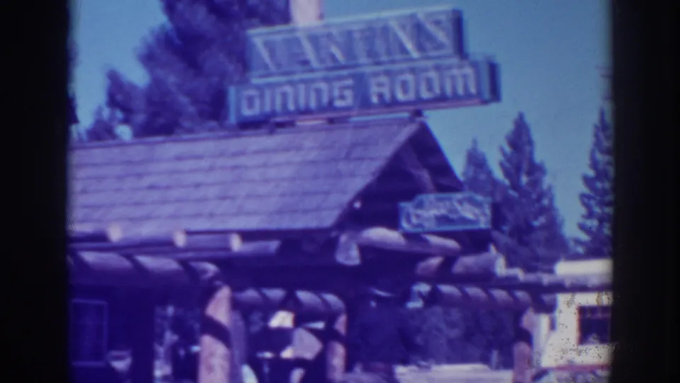 A log-fronted roadside building in El Dorado City shows a large Dining Room sign above the roofline and trees in the background.