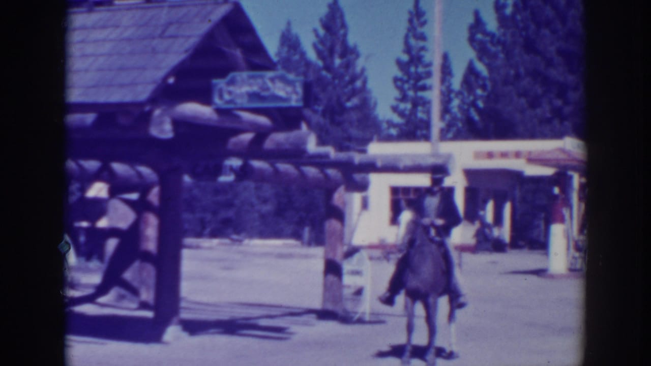 Horse and rider move away from the log structure toward an open roadside area.