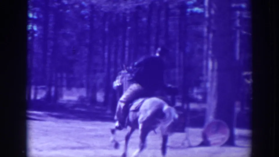 A mounted rider moves through a wooded El Dorado City setting, with strong blue-purple film color and a round sign or prop visible near the path.