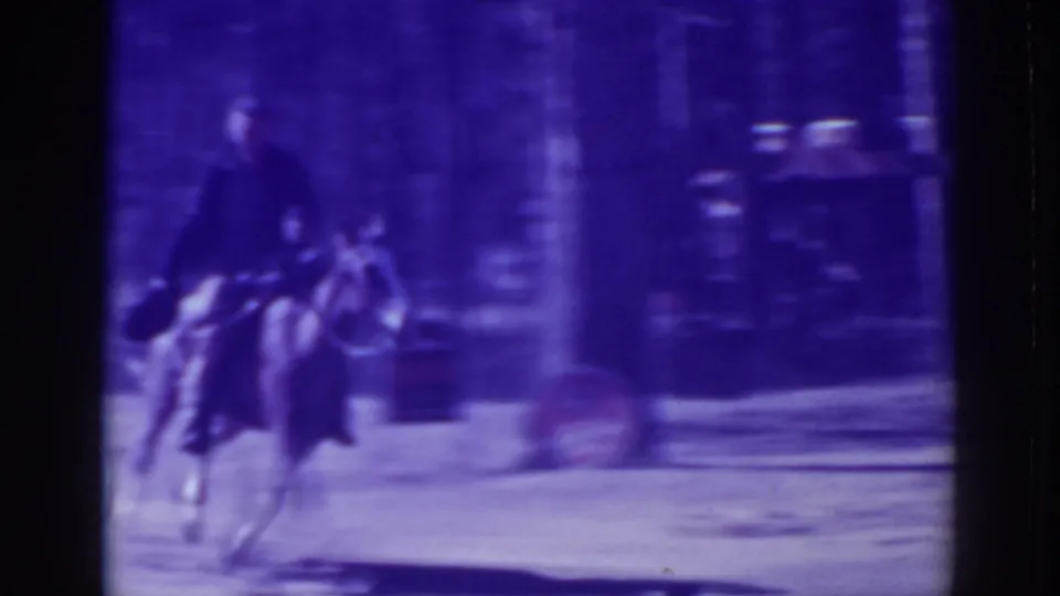 A mounted man appears to turn the horse on the dusty road, with blurred roadside structures and forest shadows behind him.
