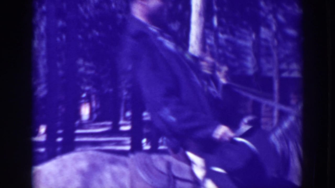 Man on horseback near trees and a building, seen in purple-tinted 8mm footage.