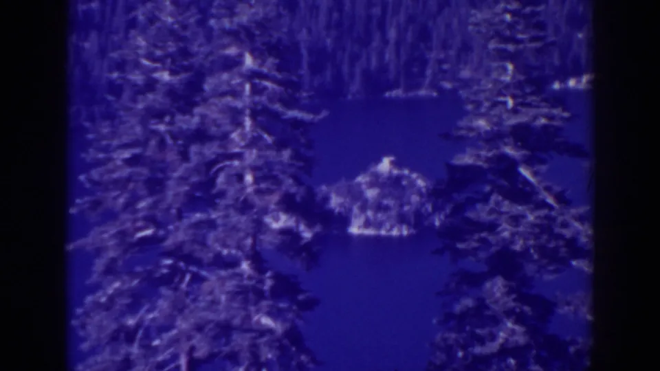 A visitor-shot 8mm view from Inspiration Point shows pine trees, calm blue water, and the rocky island within Emerald Bay.