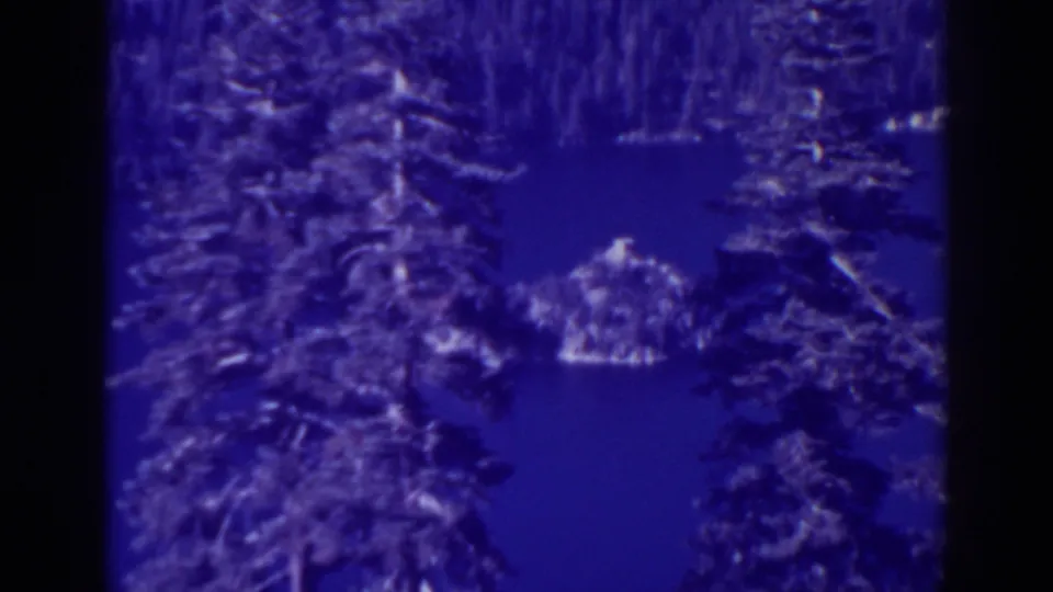 Emerald Bay landscape remains framed by pines, with the lake, small island or outcrop, and distant wooded shore visible in blue-tinted 8mm footage.