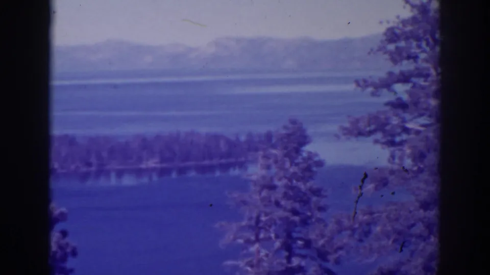The wide Emerald Bay view continues, with blue lake water, hazy mountain ridges, and trees along the foreground edge.
