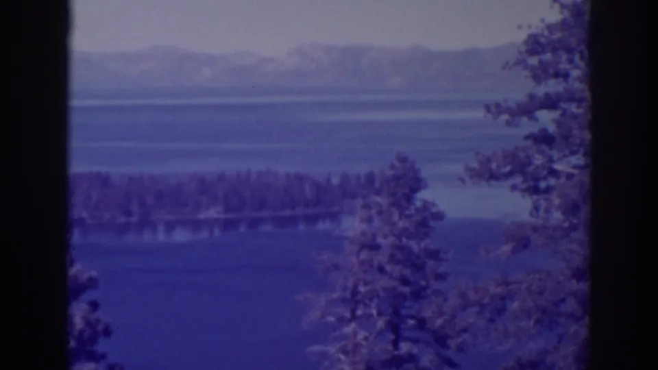 Emerald Bay lake scene framed by tall evergreens, with a forested island in the middle distance and mountains beyond the water.