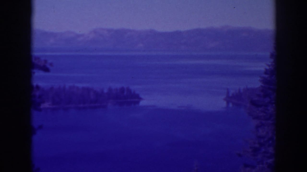 Blue-toned lake view with island silhouette, mountain ridge, trees, and dark vertical framing.