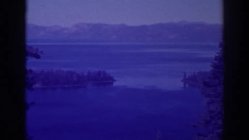 1938 Emerald Bay footage with a blue color cast, showing lake water, a wooded island, distant ridges, tree edges, and a dark central divider.