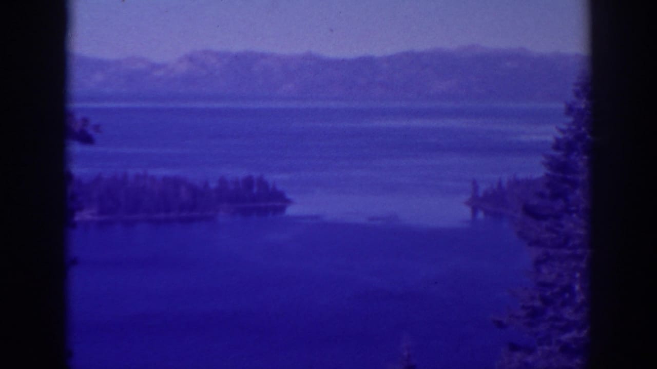 Blue lake and distant mountains seen through dark vertical frame edges.