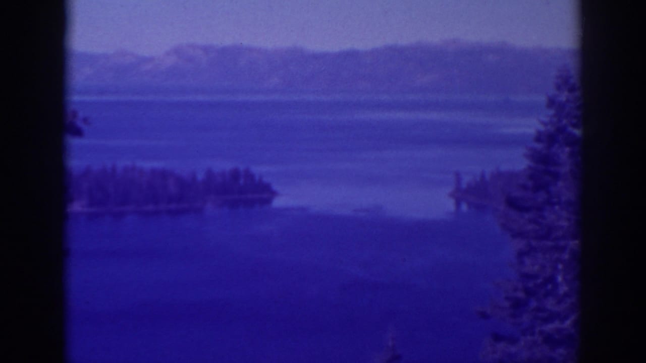 Emerald Bay, California appears in a blue-cast 8mm frame with wooded islands, calm water, and distant mountain ridges.
