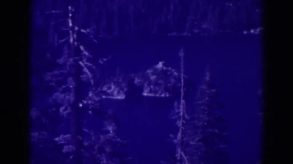 Blue-cast 1938 home-movie frame showing lake water, foreground evergreens, small islands, and a wooded shoreline at Emerald Bay.