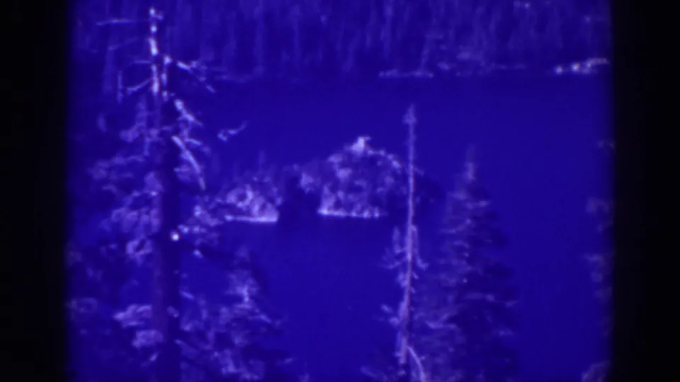 1938 Emerald Bay home-movie frame showing deep blue lake water, evergreens, and a small island or rocky feature near the center.