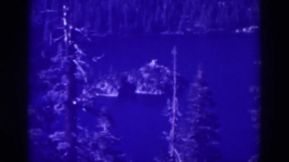 1938 Emerald Bay home-movie frame holding on the lake, evergreen trees, and a small island or rocky feature in blue-tinted color.